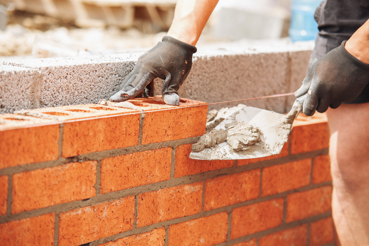 Skilled bricklayer laying bricks with trowel on construction site