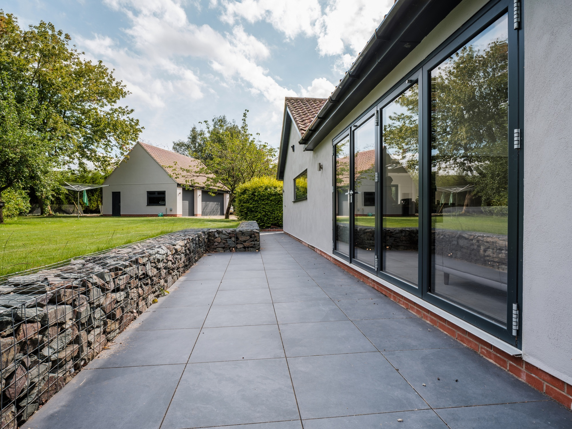 Luxury home with bifold doors leading to contemporary landscaped gardens with patio and gabian walls