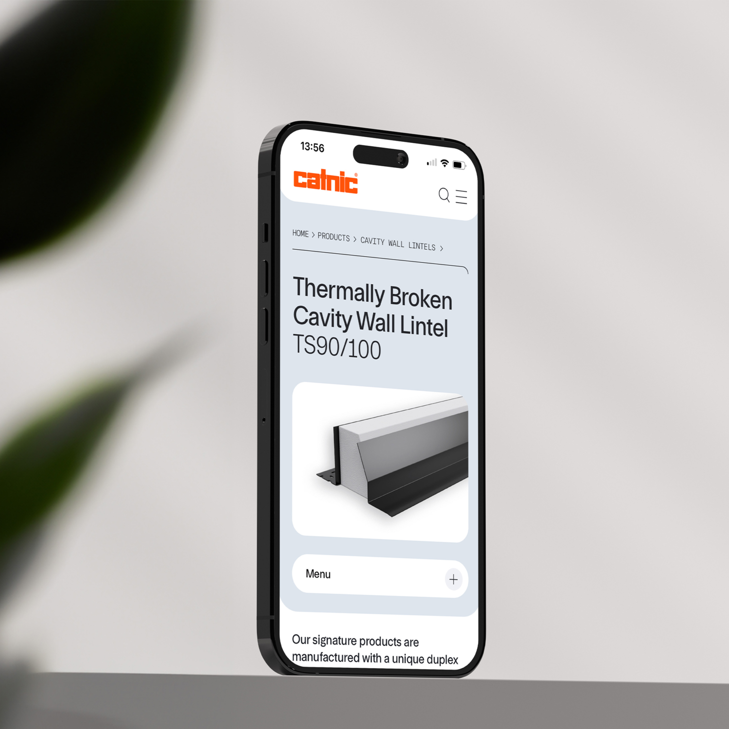 A smartphone displays a webpage featuring "Thermally Broken Cavity Wall Lintel TS90/100" with an accompanying image and text. It's set on a neutral background with a blurred plant edge.